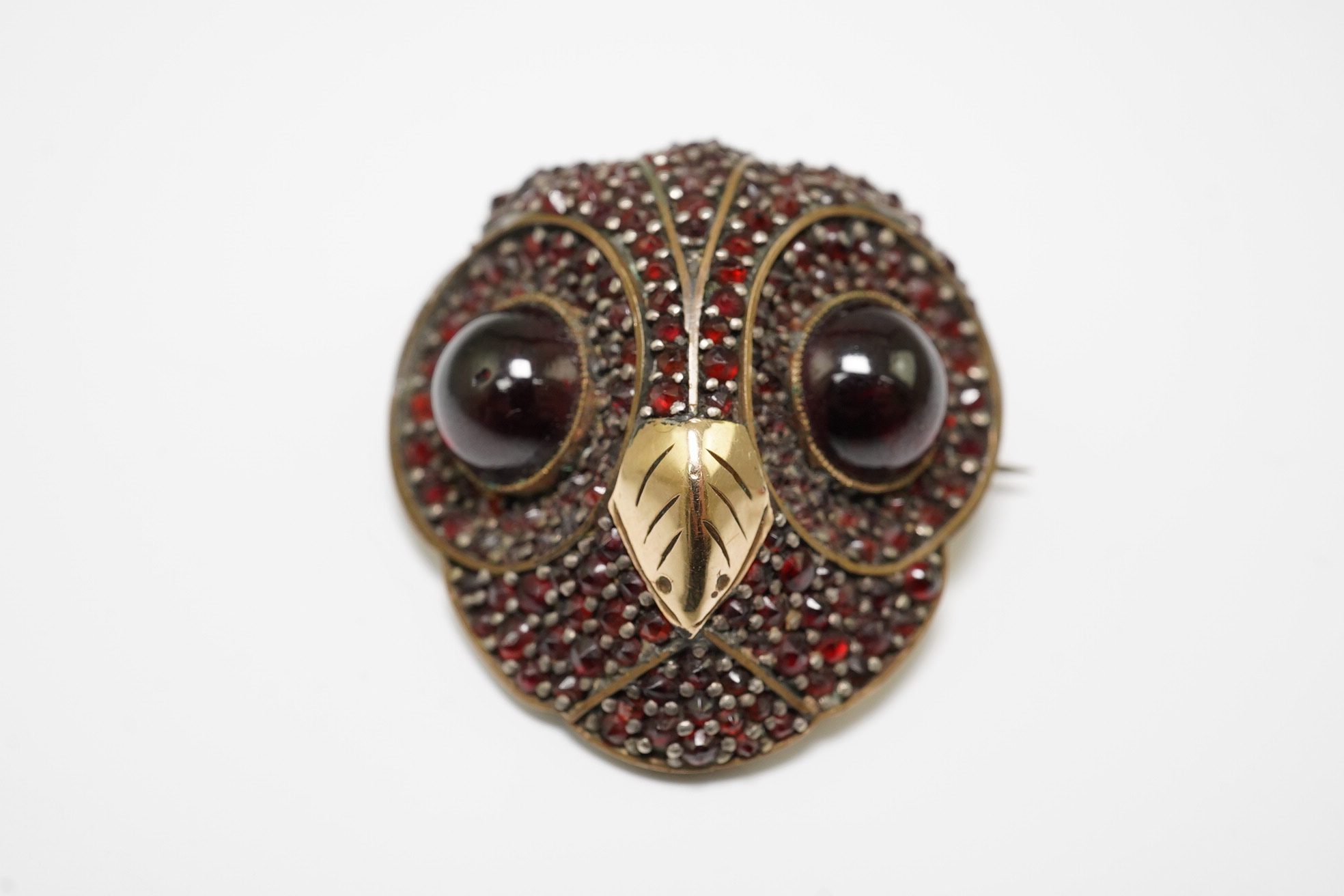 A Victorian gold overlaid base metal and pave set garnet owl's head brooch